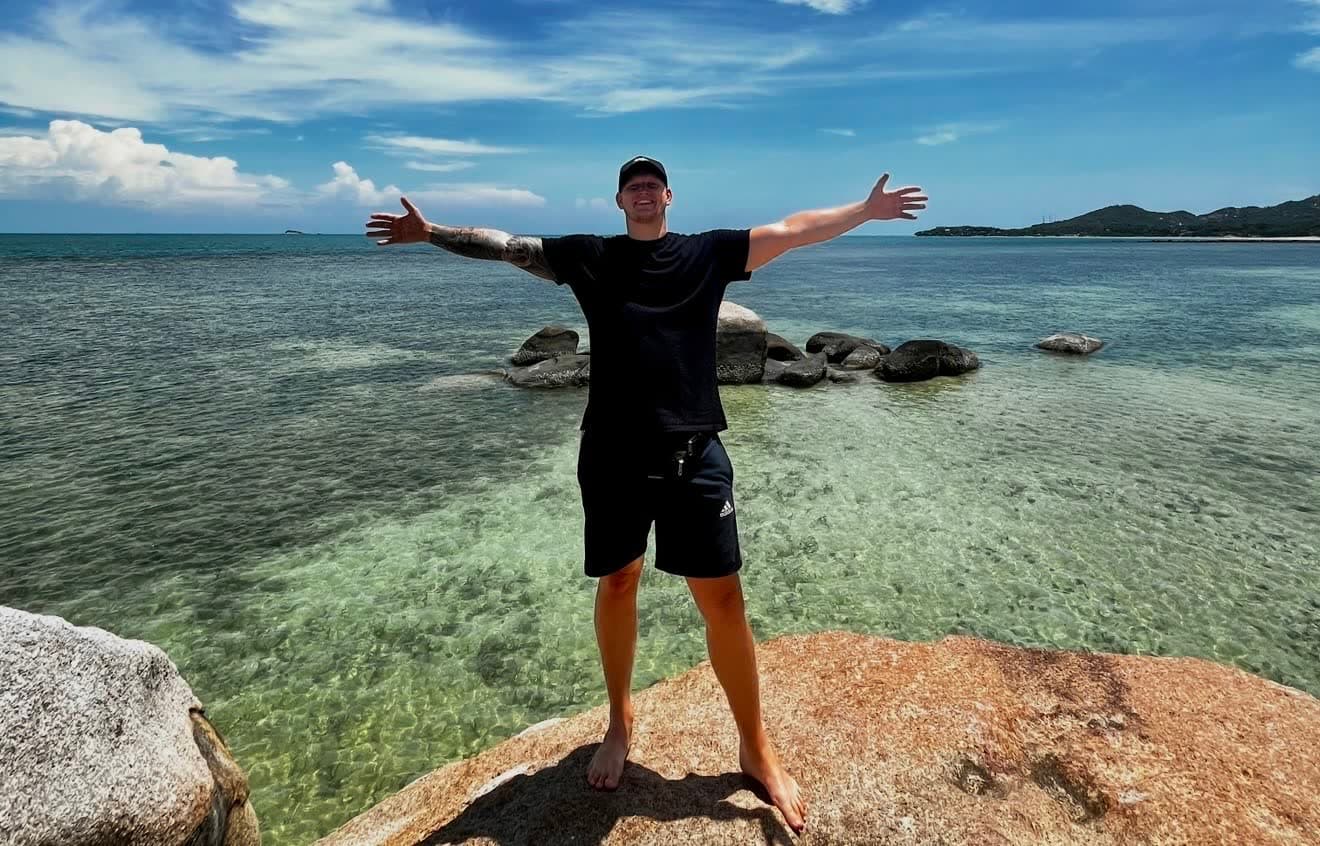 Maxi mit ausgebreiteten Armen auf einem Felsen am Meer, unterwegs zwischen zwei Kundenprojekten